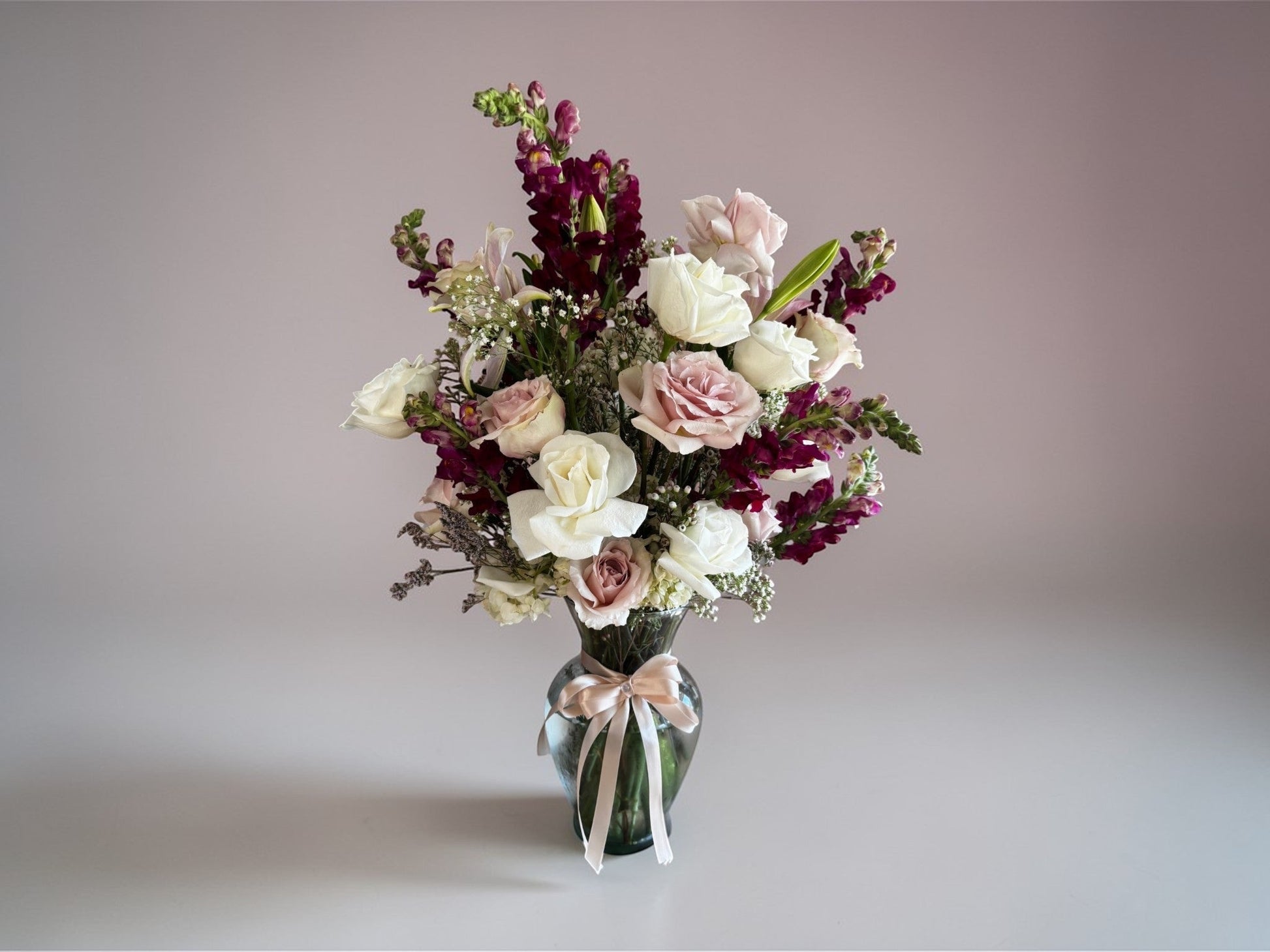 Skye Rose Floral bouquet featuring cream and mauve roses with burgundy snapdragons in a glass vase with a ribbon.