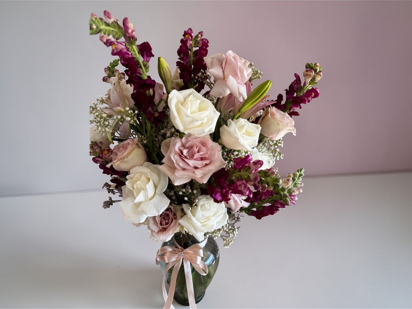 Skye Rose Floral Sophisticated Mauve bouquet with cream and dusty mauve roses and burgundy snapdragons in a glass vase.