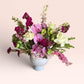 Skye Rose Floral Plum Essence arrangement featuring pink orchids, white roses, and plum calla lilies in a white vase.