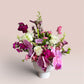 Skye Rose Floral Plum Essence arrangement featuring purple orchids, calla lilies, and white roses in a white pedestal vase