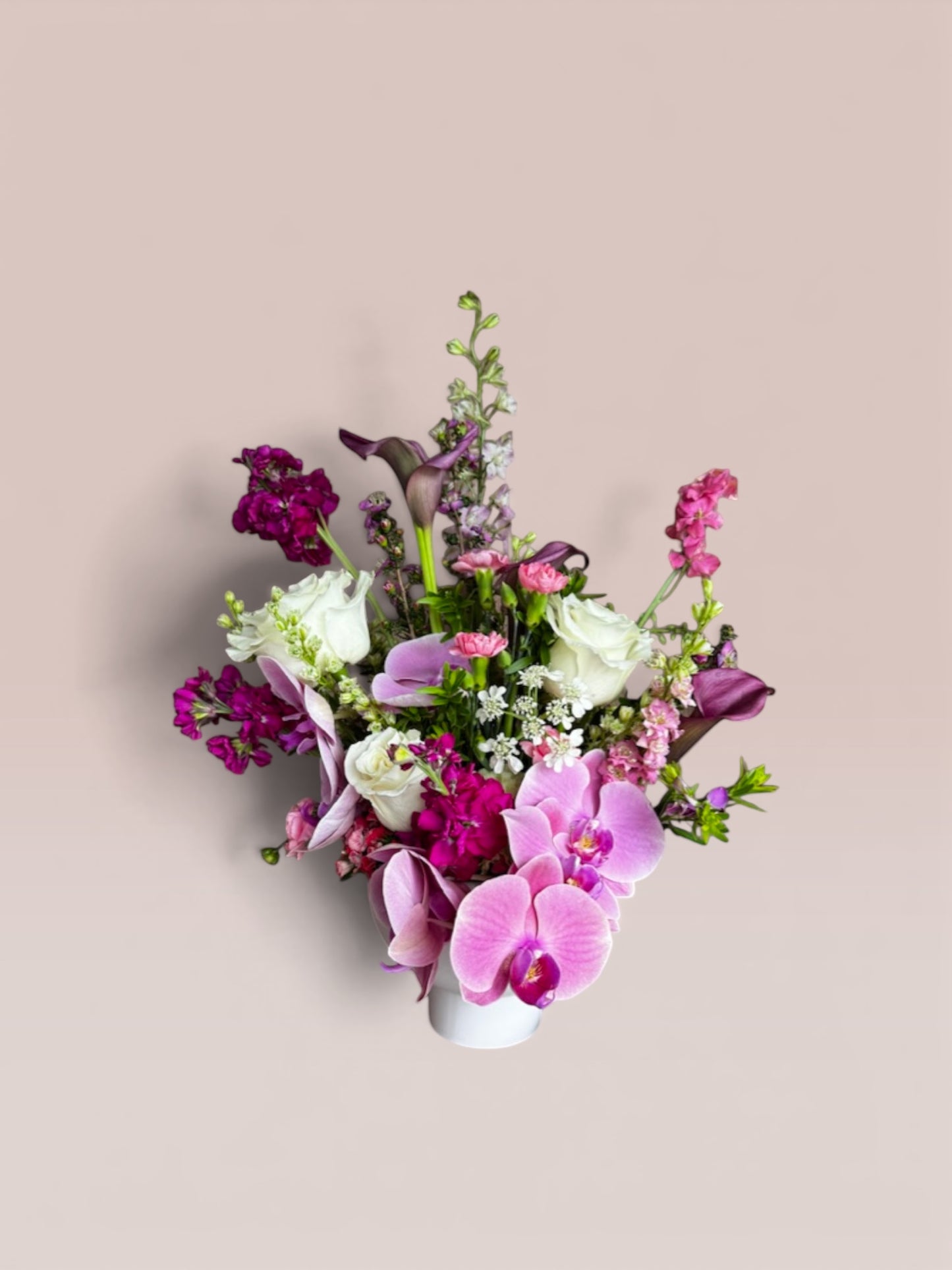 Skye Rose Floral Plum Essence arrangement featuring pink orchids, white roses, and calla lilies in a white vessel.