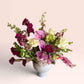 Skye Rose Floral Plum Essence arrangement featuring pink orchids, white roses, and plum calla lilies in a white vessel.