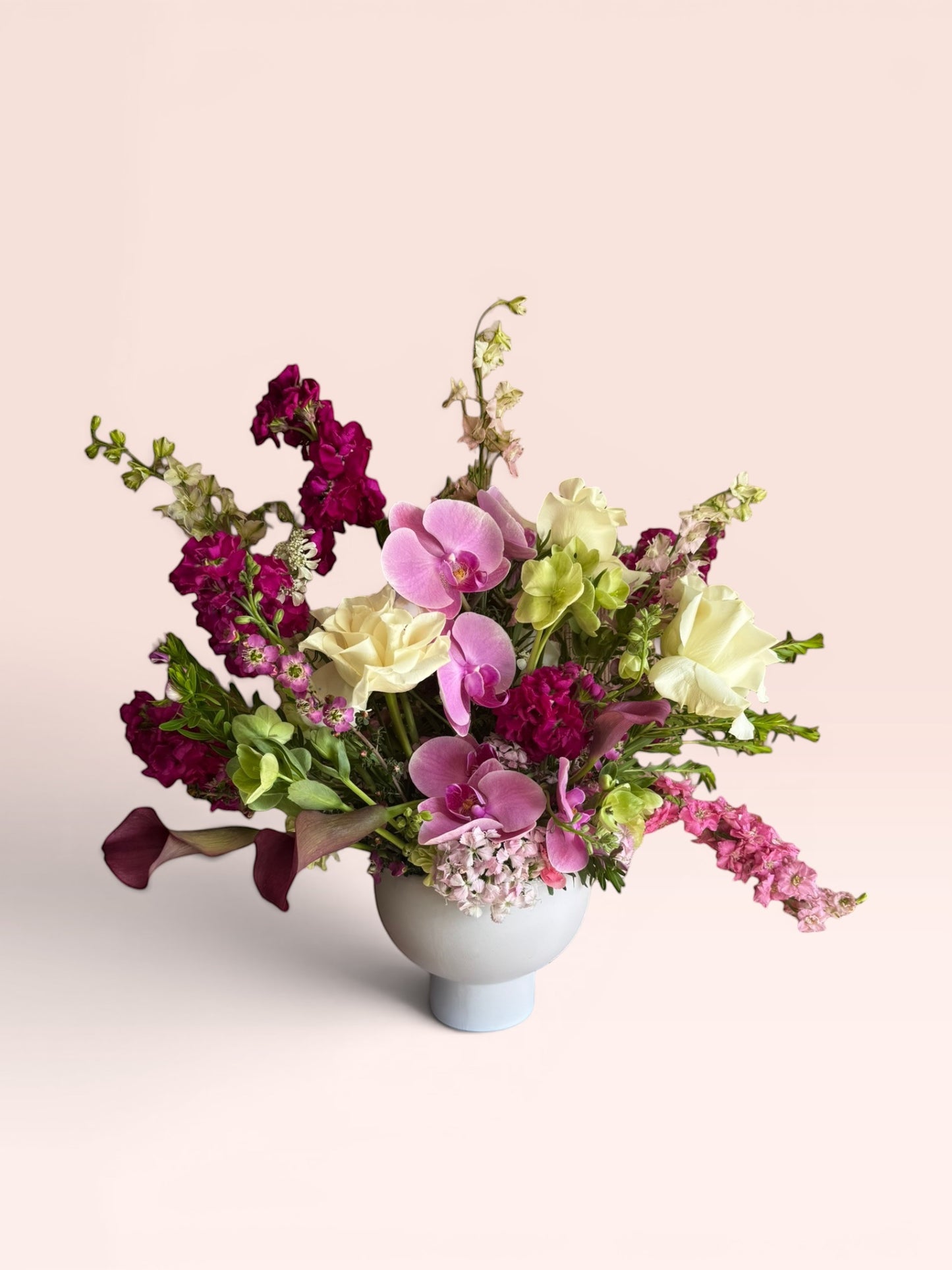 Skye Rose Floral Plum Essence arrangement featuring pink orchids, white roses, and plum calla lilies in a white vessel.
