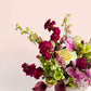 Skye Rose Floral Plum Essence arrangement with orchids, calla lilies, and roses in a modern white pedestal vase.