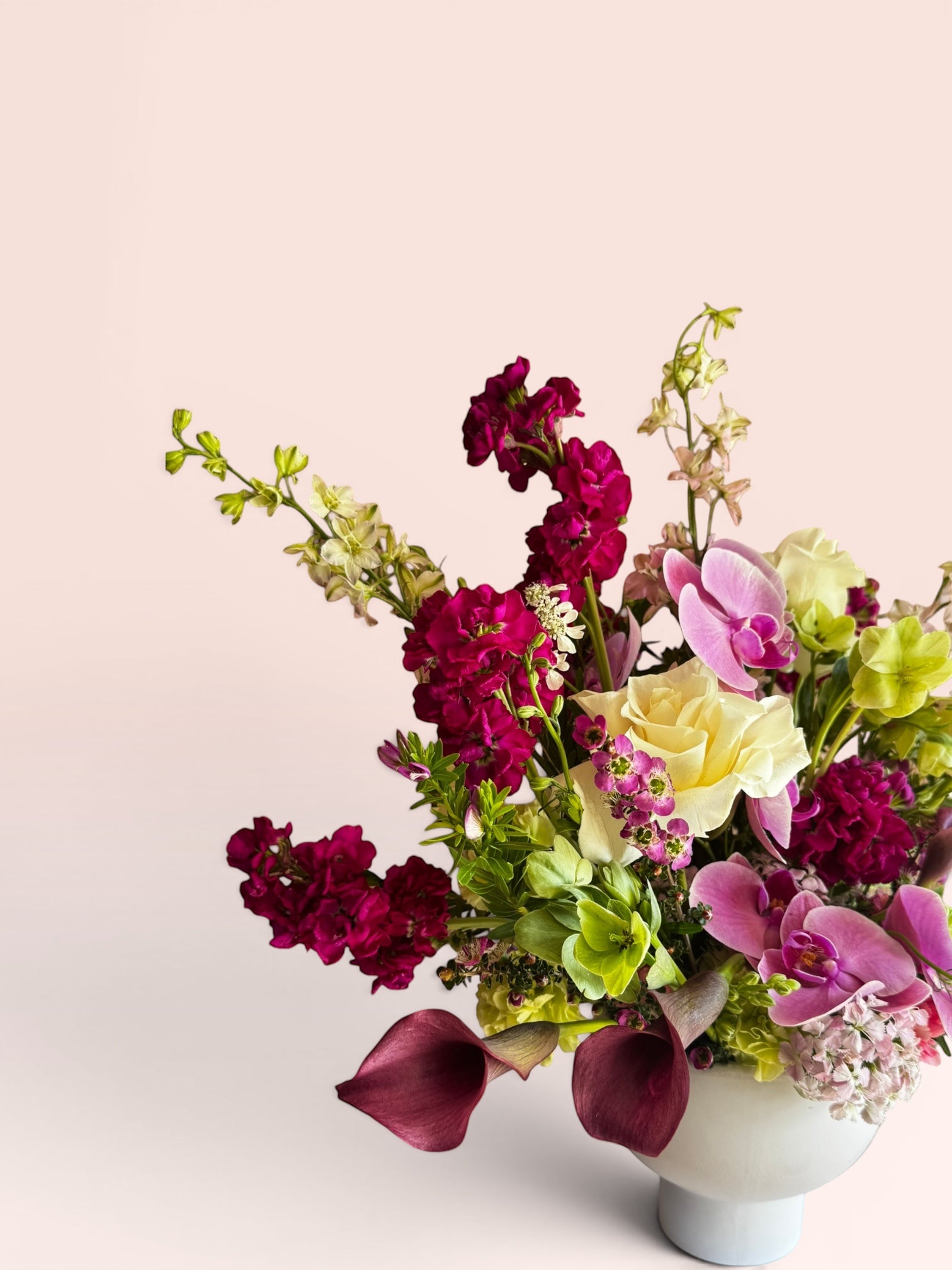 Skye Rose Floral Plum Essence arrangement with orchids, calla lilies, and roses in a modern white pedestal vase.