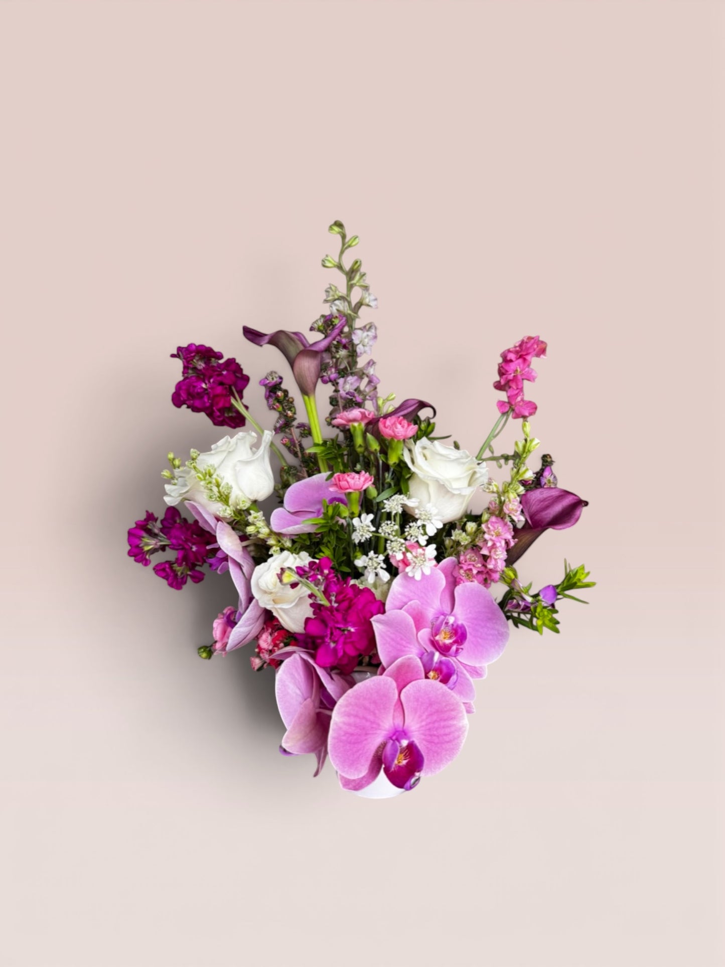 Skye Rose Floral Plum Essence arrangement with pink Phalaenopsis orchids, calla lilies, and white roses in a white vase.